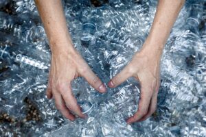 Two hands are arranging a pile of empty, crumpled clear plastic bottles, highlighting the importance of plastic recycling in Singapore.