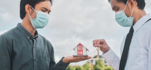 Two men wearing masks; one holds a model house, the other offers a key toward him, suggesting a real estate transaction outdoors—possibly referencing procedures similar to those at Caveat Lodge Singapore.