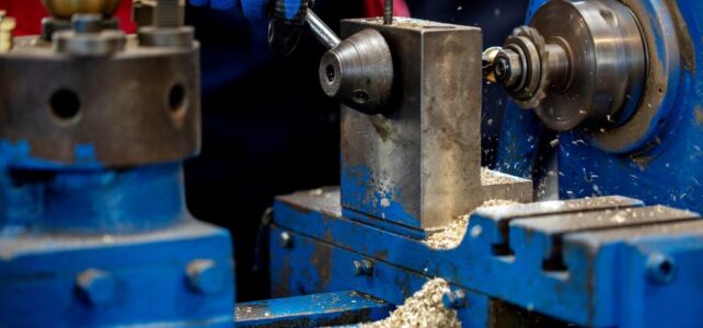 A person operates a blue metal lathe, shaping a metal piece while metal shavings accumulate—demonstrating the precision manufacturing seen at leading Metal Injection Molding Companies in Singapore.